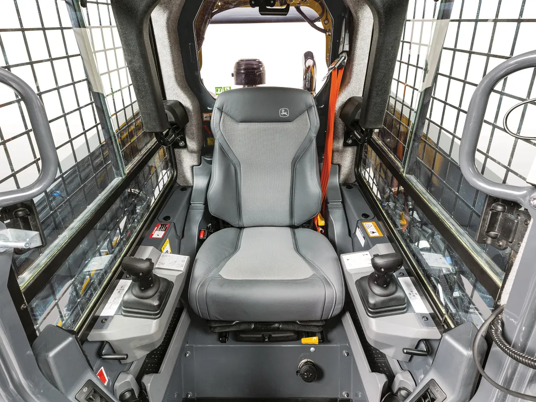 John Deere 333 P-Tier gallery — Interior cab view of a skid steer loader showing a central padded operator seat, protective side grid panels, and dual joystick controls on both armrests
